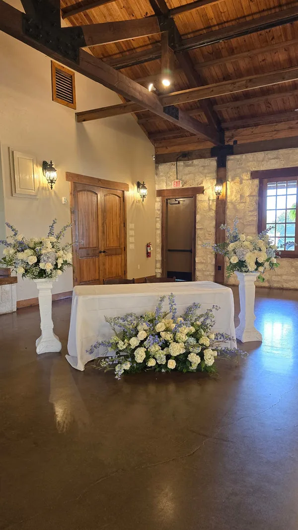 White and pale-blue floral arrangements on two pedestals and in front of a white-covered table