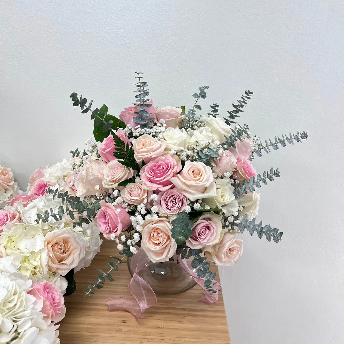 Blush, pink and ivory roses with white blooms and greenery in a clear vase