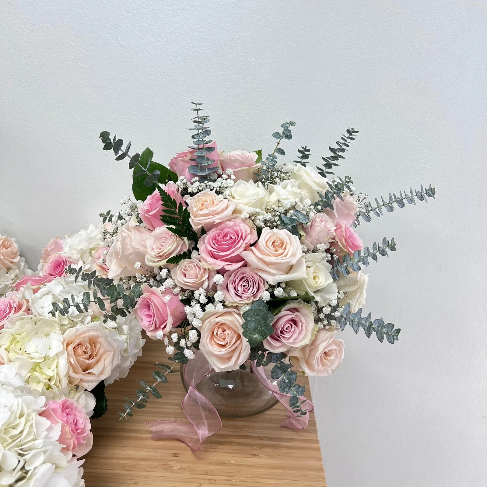 Blush, pink and ivory roses with white blooms and greenery in a clear vase