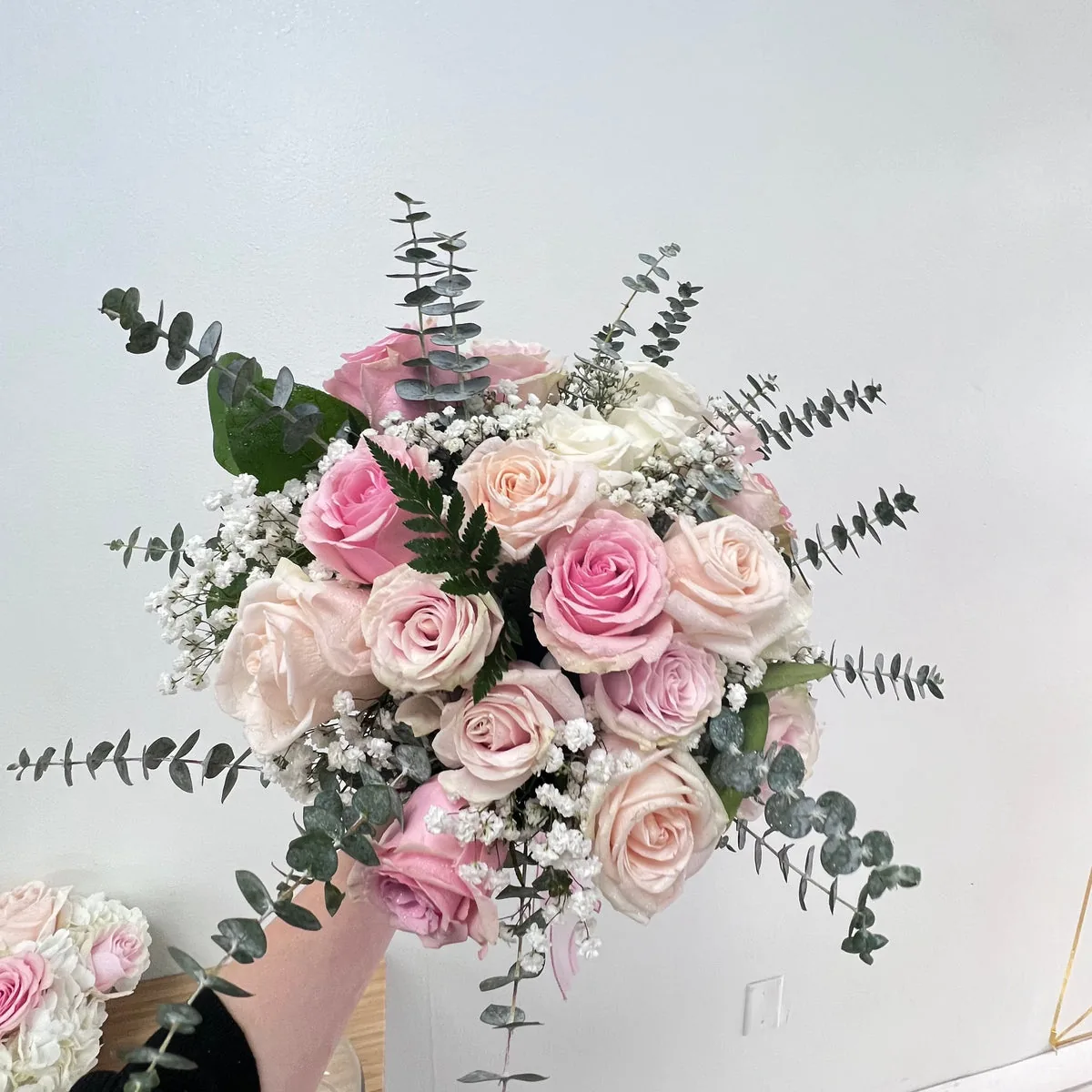 Pink, blush and ivory roses with delicate white flowers and eucalyptus foliage held against a pale wall